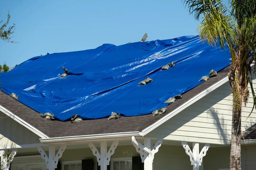 A large roof covered in two tarps weighed down with sandbags.